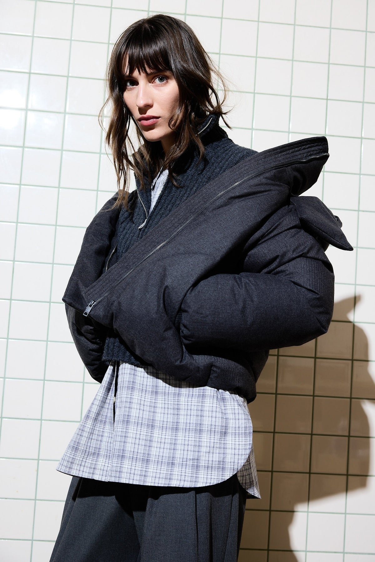 Kvinna i mörkgrå vadderad vinterjacka mot kakelvägg